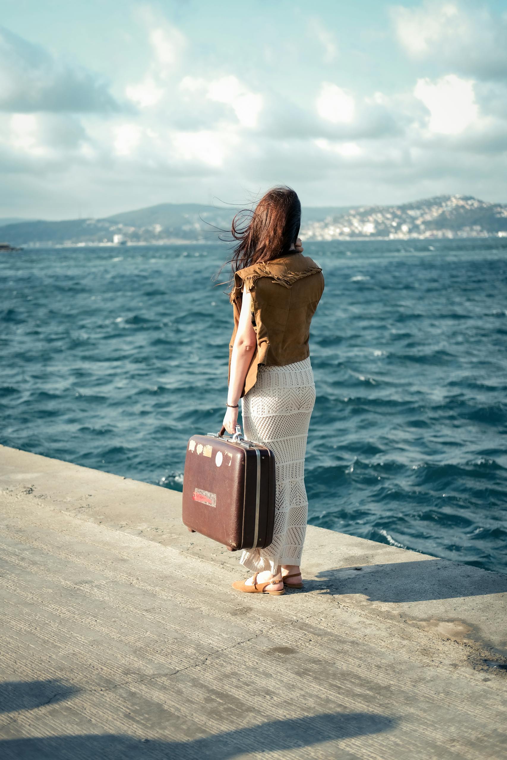 How to move abroad as an American - a woman stands on a beach promenade with a suitcase by the sea