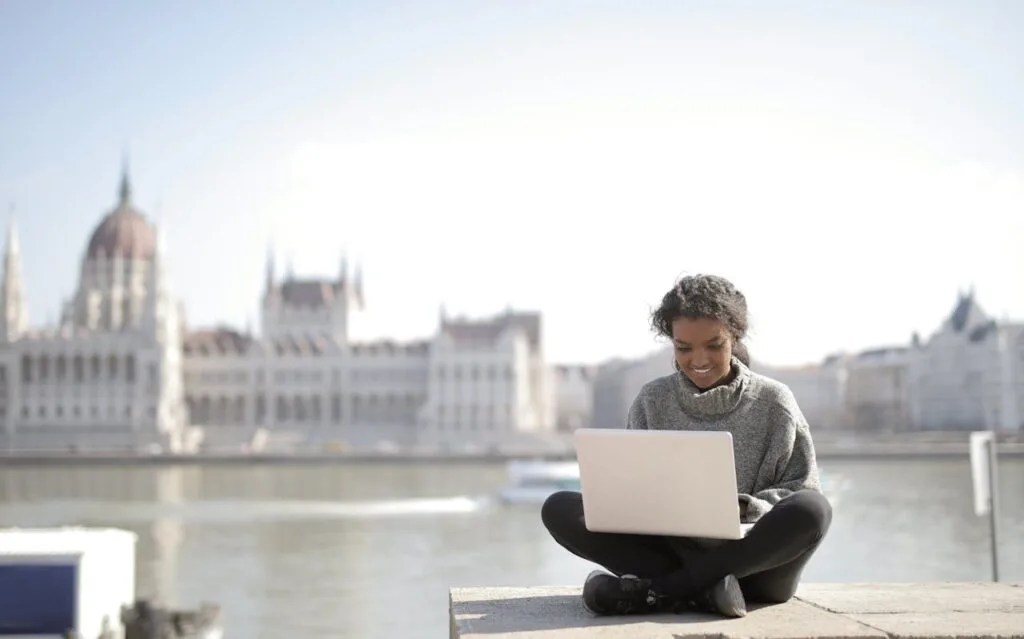 Black woman working remotely on laptop in European city, the type of digital nomad SafetyWing Nomad Insurance is designed for