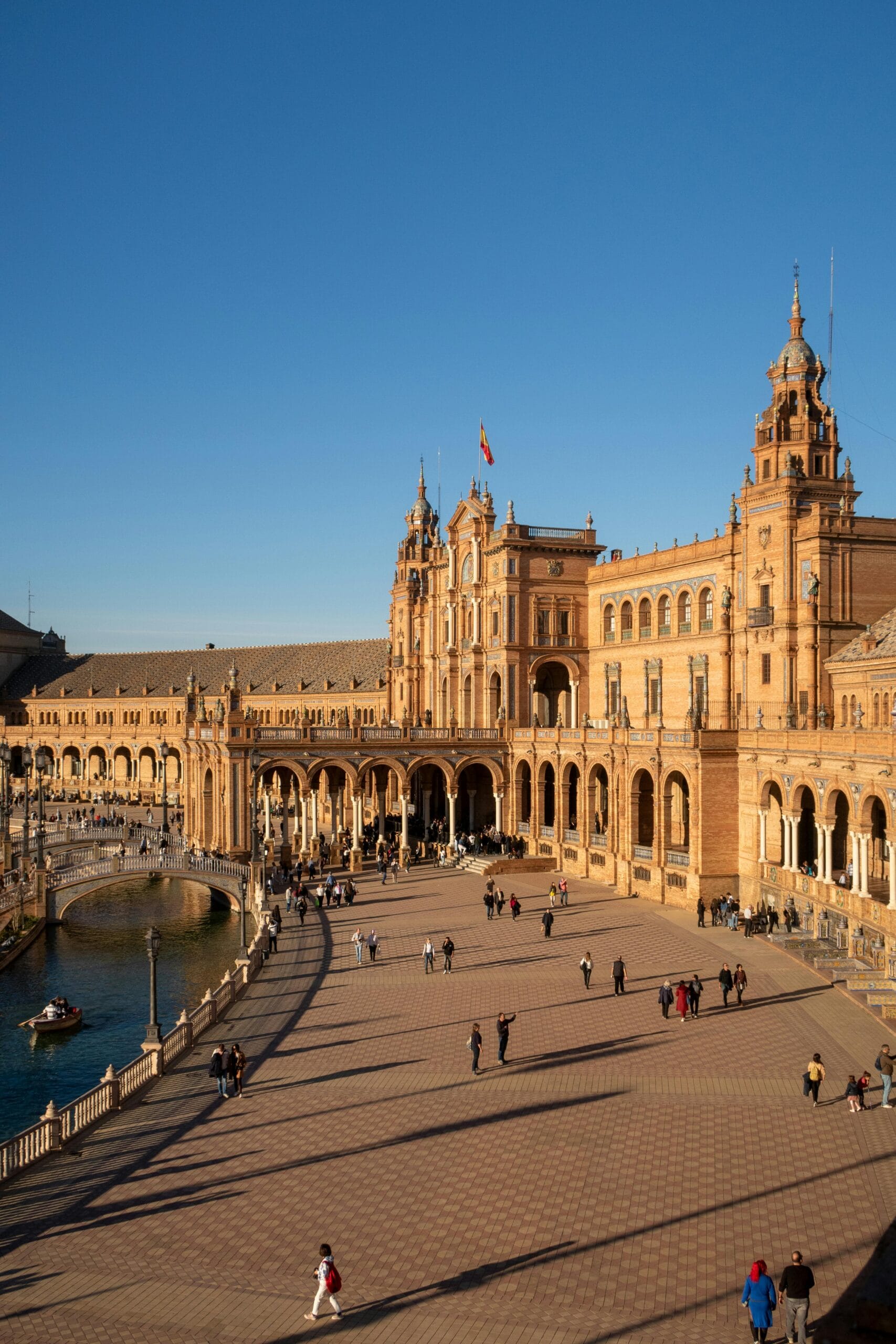 Moving to Spain as an American - a smiling young man with a suitcase and map standing in a sunny Spanish city street with colorful buildings and cafes.