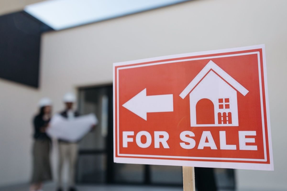 Sell Everything and Move Abroad: The 7 Real Numbers From My Move 2 Red for sale sign with an arrow outside a modern house, the first step to sell everything and move abroad
