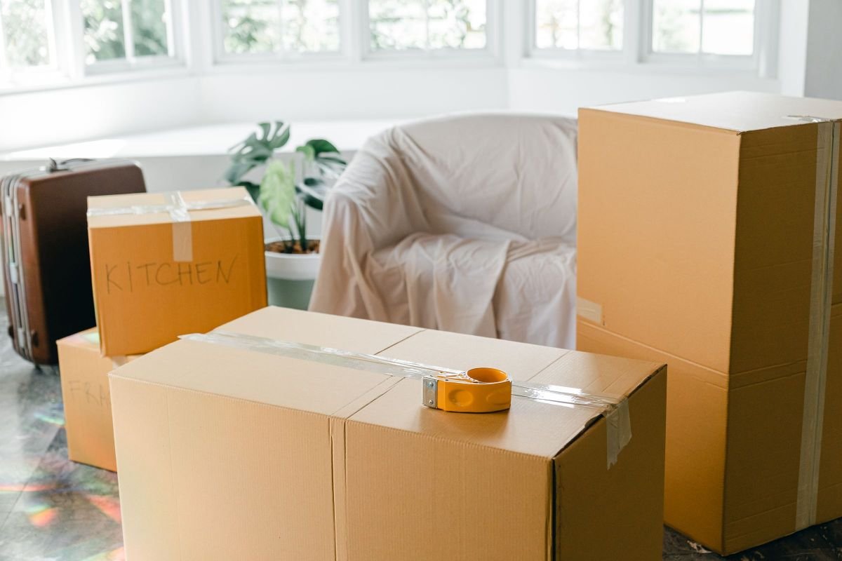 Sell Everything and Move Abroad: The 7 Real Numbers From My Move 4 Taped cardboard moving boxes, a suitcase and a covered armchair in a bright room with large windows