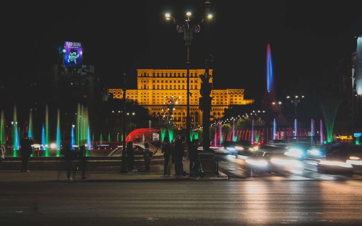 Living in Romania as an American: 9 Essential Things to Know (2026) 2 Colorful fountains and lit buildings along a Bucharest boulevard at night