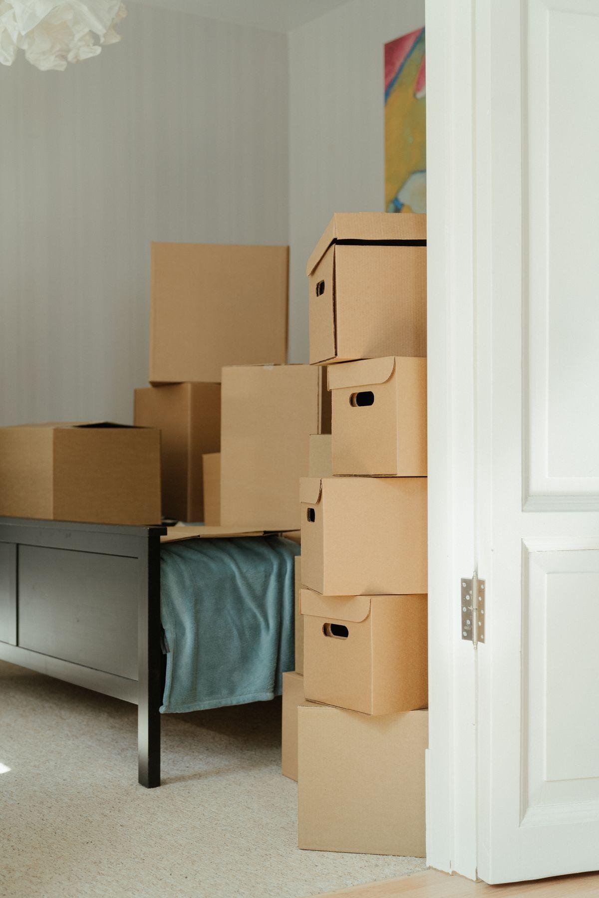Stacked cardboard moving boxes in a bedroom beside an open white door