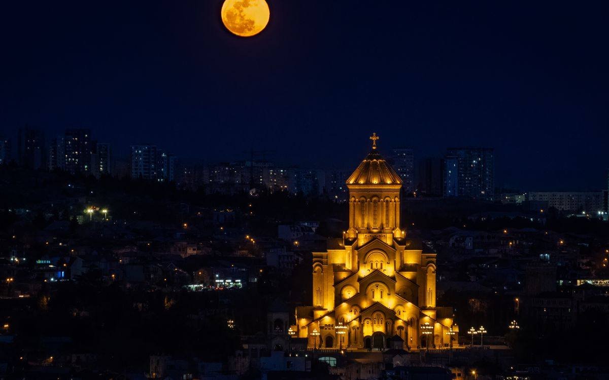 Holy Trinity Cathedral lit in gold at night under a full moon over Tbilisi Georgia