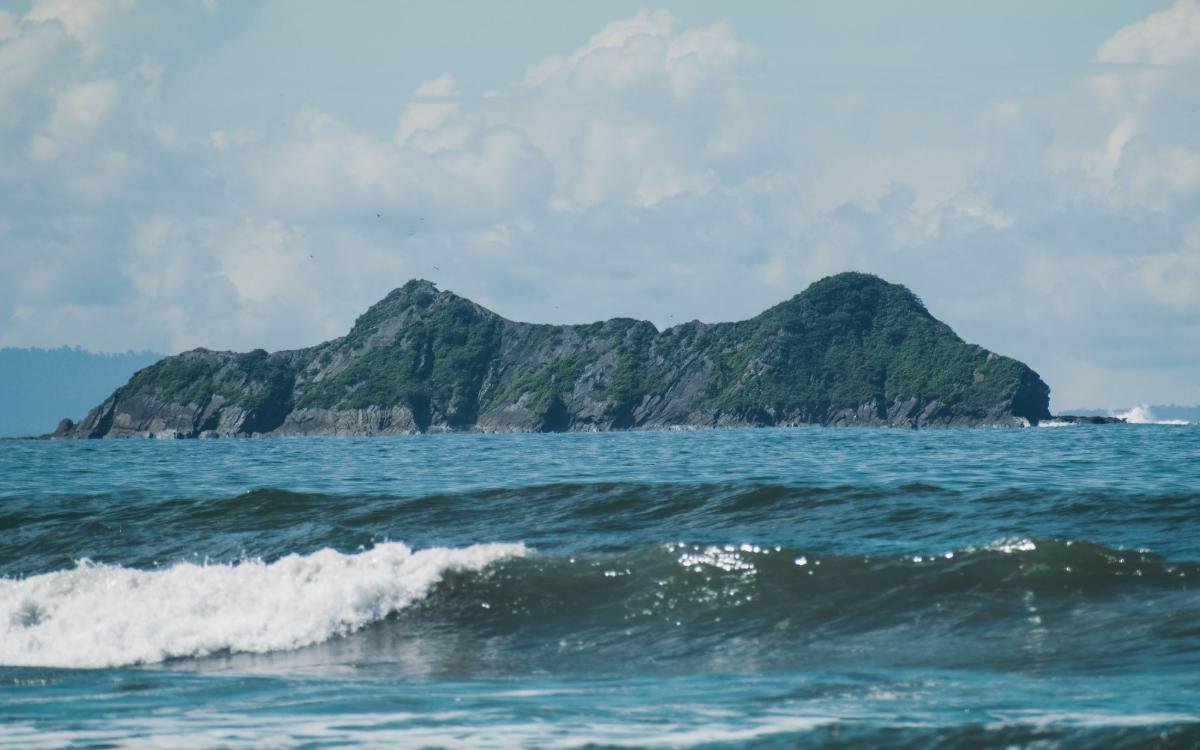 Costa Rica Digital Nomad Visa: 7 Key Requirements (2026) 4 Waves breaking on the shore at Uvita with a forested island offshore on the Pacific coast of Costa Rica